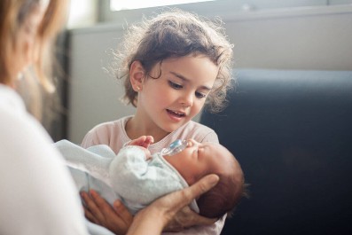 mother hands newborn to her new big sister Young girl holds baby sister