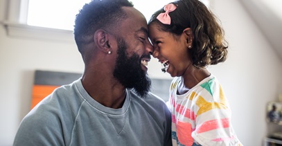 Father and young daughter facing each other with their foreheads together laughing