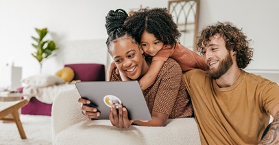 interracial couple with daughter draped over mom's shoulders looking at ipad